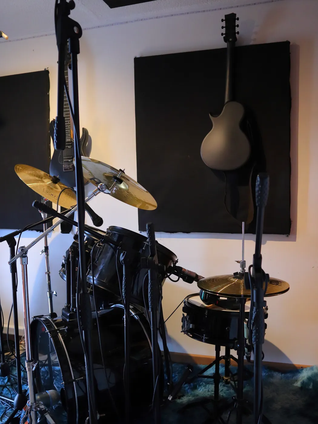 Estudio Clancy: sala de grabación con batería, micrófonos en pedestal, guitarras colgadas y paneles acústicos